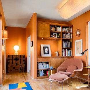 Inspiration for a small modern home office and library in Raleigh with a reading nook, orange walls and light hardwood flooring.