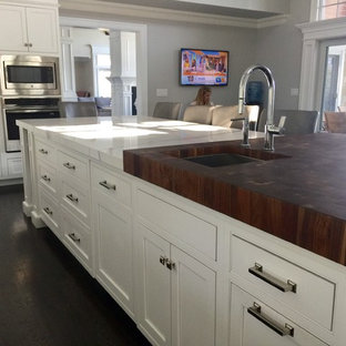 Idées déco pour une grande arrière-cuisine classique en U avec un sol marron, un évier encastré, un placard à porte plane, des portes de placard blanches, un plan de travail en verre, une crédence blanche, une crédence en feuille de verre, un électroménager encastrable, un sol en bois foncé et un îlot central.