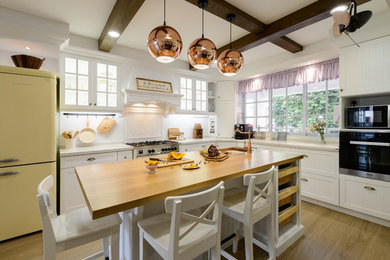 Inspiration for a country l-shaped separate kitchen in Singapore with an undermount sink, shaker cabinets, white cabinets, wood benchtops, white splashback, coloured appliances, light hardwood floors, with island, beige floor and beige benchtop.