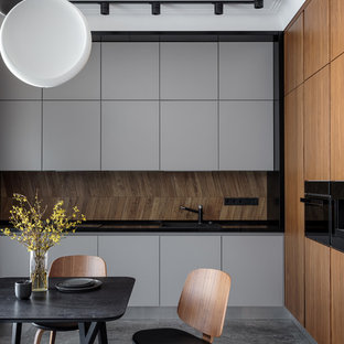 На фото: кухня в современном стиле с плоскими фасадами, серыми фасадами, коричневым фартуком, черной техникой, серым полом, черной столешницей и обеденным столом с