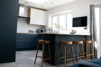 Mid-sized modern u-shaped kitchen in Other with flat-panel cabinets, blue cabinets, solid surface benchtops, white splashback, black appliances, a peninsula and white benchtop.