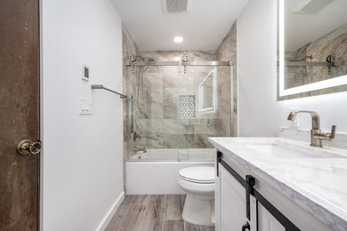 Mid-sized minimalist multicolored tile laminate floor, gray floor and double-sink bathroom photo in Seattle with white cabinets, a one-piece toilet, white walls, quartzite countertops, white countertops and a niche