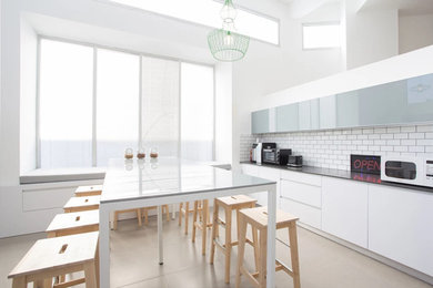 Mid-sized elegant single-wall concrete floor and beige floor eat-in kitchen photo in Los Angeles with flat-panel cabinets, white cabinets, white backsplash, subway tile backsplash and an island