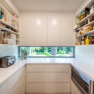 Design ideas for an expansive beach style u-shaped kitchen pantry in Melbourne with an undermount sink, flat-panel cabinets, white cabinets, quartz benchtops, window splashback, stainless steel appliances, medium hardwood floors and white benchtop.