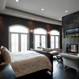 Inspiration for a large transitional master bedroom in San Francisco with black walls, painted wood floors, a hanging fireplace, a stone fireplace surround and black floor.