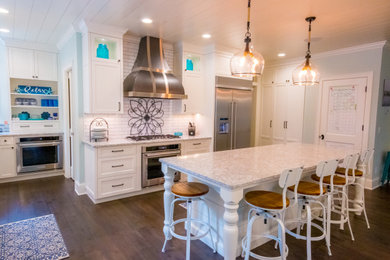 Example of a large transitional l-shaped dark wood floor, brown floor and shiplap ceiling eat-in kitchen design in Minneapolis with a farmhouse sink, shaker cabinets, white cabinets, quartz countertops, white backsplash, subway tile backsplash, stainless steel appliances, an island and beige countertops