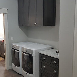 Design ideas for a medium sized shabby-chic style galley separated utility room in Minneapolis with a belfast sink, flat-panel cabinets, grey cabinets, granite worktops, grey walls, vinyl flooring, a side by side washer and dryer, grey floors and white worktops.