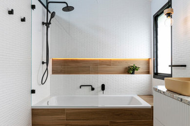 This is an example of a mid-sized beach style kids bathroom in Sydney with white cabinets, a drop-in tub, a shower/bathtub combo, a two-piece toilet, white tile, ceramic tile, white walls, ceramic floors, a vessel sink, terrazzo benchtops, brown floor, an open shower, multi-coloured benchtops, a shower seat, a double vanity, a floating vanity and vaulted.