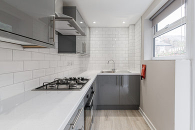 Inspiration for a medium sized modern grey and white l-shaped enclosed kitchen in Other with a built-in sink, flat-panel cabinets, grey cabinets, limestone worktops, white splashback, metro tiled splashback, stainless steel appliances, light hardwood flooring, no island and white worktops.