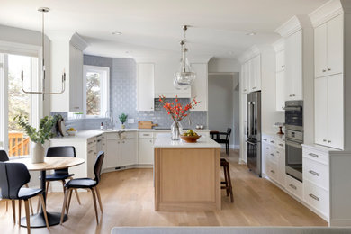 Example of a large classic u-shaped light wood floor eat-in kitchen design in Minneapolis with an undermount sink, shaker cabinets, white cabinets, quartz countertops, gray backsplash, subway tile backsplash, stainless steel appliances, an island and white countertops