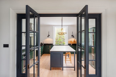 This is an example of a mid-sized transitional u-shaped separate kitchen in Devon with a drop-in sink, shaker cabinets, green cabinets, solid surface benchtops, white splashback, white appliances, medium hardwood floors, with island, brown floor and white benchtop.