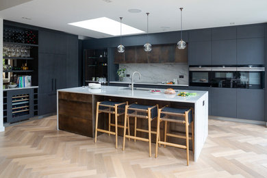 Inspiration for a contemporary l-shaped open plan kitchen in London with an integrated sink, flat-panel cabinets, black cabinets, quartzite benchtops, white splashback, stone slab splashback, black appliances, with island and white benchtop.