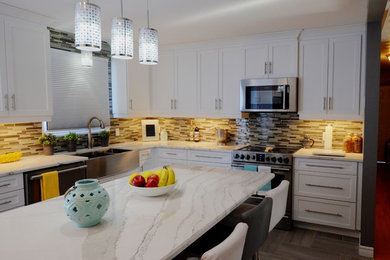 Inspiration for a mid-sized transitional galley ceramic tile kitchen remodel in Toronto with a farmhouse sink, shaker cabinets, white cabinets, quartzite countertops, gray backsplash, glass tile backsplash, stainless steel appliances and an island