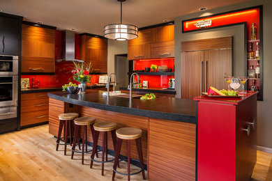 Inspiration for a mid-sized contemporary l-shaped eat-in kitchen in Portland with an undermount sink, flat-panel cabinets, medium wood cabinets, granite benchtops, red splashback, glass sheet splashback, panelled appliances, light hardwood floors and with island.