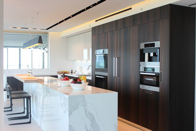 Open concept kitchen - mid-sized contemporary single-wall white floor open concept kitchen idea in Miami with a single-bowl sink, flat-panel cabinets, white cabinets, marble countertops, white backsplash, stone slab backsplash, stainless steel appliances and an island