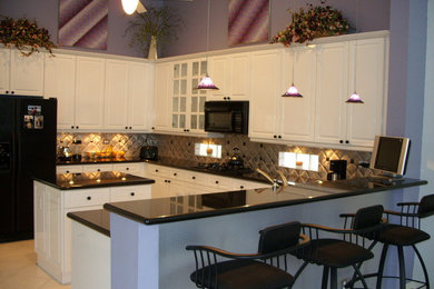 Mid-sized trendy u-shaped ceramic tile and beige floor open concept kitchen photo in Miami with raised-panel cabinets, white cabinets, granite countertops, metallic backsplash, metal backsplash, black appliances, an island and black countertops