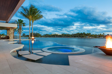 Design ideas for a large tropical backyard custom-shaped infinity pool in Miami with natural stone pavers and a hot tub.