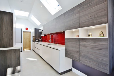 Photo of a large contemporary galley open plan kitchen in London with flat-panel cabinets, medium wood cabinets, quartzite benchtops, red splashback, glass sheet splashback, stainless steel appliances and a peninsula.