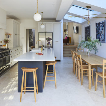 Open plan cream kitchen with dark blue island, glazed units and brass fixings
