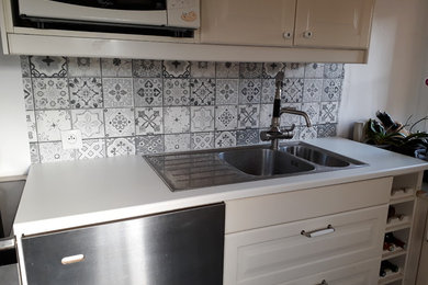 Exemple d'une petite cuisine linéaire nature fermée avec un évier intégré, un placard à porte affleurante, des portes de placard blanches, un plan de travail en stratifié, une crédence grise, une crédence en céramique, un électroménager en acier inoxydable, sol en stratifié, aucun îlot, un sol noir et un plan de travail blanc.