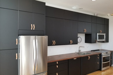 Example of a small minimalist single-wall light wood floor and brown floor eat-in kitchen design in Seattle with a single-bowl sink, flat-panel cabinets, black cabinets, laminate countertops, stainless steel appliances and brown countertops