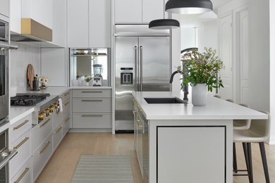 Mid-sized minimalist single-wall light wood floor and white floor open concept kitchen photo in Toronto with an undermount sink, raised-panel cabinets, white cabinets, white backsplash, porcelain backsplash, stainless steel appliances, an island and white countertops