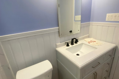 Small arts and crafts 3/4 gray tile laminate floor, gray floor, single-sink and wainscoting bathroom photo in New York with furniture-like cabinets, white cabinets, a two-piece toilet, blue walls, an integrated sink, quartz countertops, white countertops and a freestanding vanity