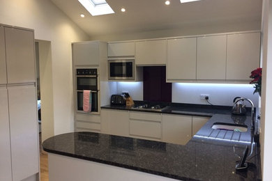 This is an example of a large contemporary u-shaped eat-in kitchen in Other with a drop-in sink, flat-panel cabinets, beige cabinets, granite benchtops, black splashback, glass sheet splashback, stainless steel appliances and no island.