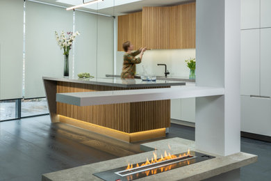 Photo of a medium sized contemporary grey and white single-wall open plan kitchen in London with an integrated sink, flat-panel cabinets, medium wood cabinets, composite countertops, black appliances, an island, grey worktops and feature lighting.