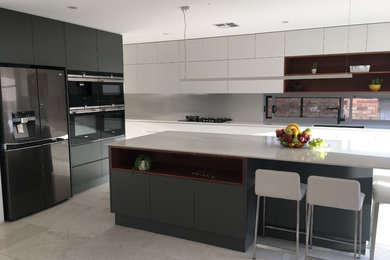 This is an example of a large contemporary u-shaped open plan kitchen in Sydney with an undermount sink, white cabinets, quartz benchtops, white splashback, stone slab splashback, stainless steel appliances, limestone floors, with island and beige floor.