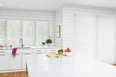Open concept kitchen - large transitional l-shaped light wood floor open concept kitchen idea in New York with a double-bowl sink, shaker cabinets, white cabinets, quartzite countertops, stainless steel appliances and an island