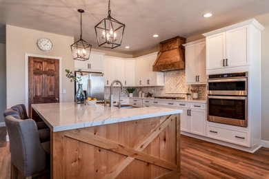 Example of a mid-sized country l-shaped vinyl floor and brown floor eat-in kitchen design with a farmhouse sink, shaker cabinets, white cabinets, quartz countertops, multicolored backsplash, marble backsplash, stainless steel appliances, an island and white countertops