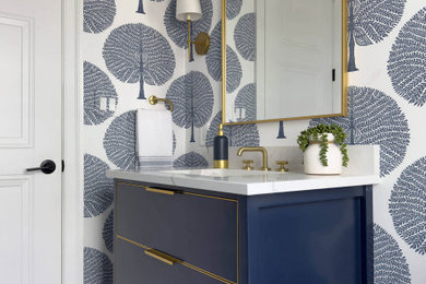 Inspiration for a small modern light wood floor, beige floor and wallpaper powder room remodel with shaker cabinets, blue cabinets, a one-piece toilet, multicolored walls, a drop-in sink, white countertops and a freestanding vanity