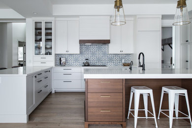 This is an example of a large transitional u-shaped eat-in kitchen in Vancouver with a farmhouse sink, shaker cabinets, white cabinets, quartz benchtops, multi-coloured splashback, porcelain splashback, panelled appliances, light hardwood floors, with island, beige floor and white benchtop.
