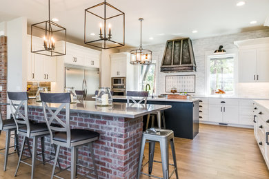Open concept kitchen - large country u-shaped light wood floor and beige floor open concept kitchen idea in Denver with a farmhouse sink, shaker cabinets, white cabinets, quartz countertops, gray backsplash, marble backsplash, stainless steel appliances, two islands and white countertops