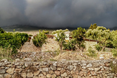 Exemple d'un grand jardin méditerranéen l'été avec un mur de soutènement, une exposition ensoleillée, une pente, une colline ou un talus et des pavés en pierre naturelle.