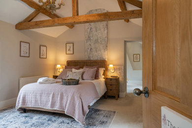 This is an example of a large rural master and grey and pink bedroom in Gloucestershire with pink walls, carpet, beige floors and exposed beams.