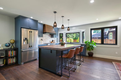Example of a mid-sized trendy l-shaped dark wood floor and brown floor eat-in kitchen design in Vancouver with an undermount sink, shaker cabinets, blue cabinets, wood countertops, beige backsplash, terra-cotta backsplash, stainless steel appliances, an island and brown countertops