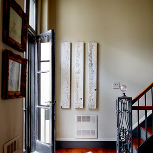 Aménagement d'une porte d'entrée éclectique de taille moyenne avec un mur beige, un sol en bois brun, une porte noire et un sol orange.