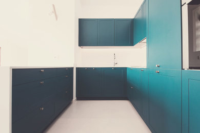 Bild på ett mellanstort funkis vit vitt kök, med en undermonterad diskho, luckor med infälld panel, blå skåp, bänkskiva i kvartsit, vitt stänkskydd, rostfria vitvaror, betonggolv, en köksö och grått golv