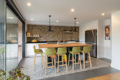 Contemporary l-shaped kitchen in Madrid with a farmhouse sink, flat-panel cabinets, white cabinets, wood benchtops, brown splashback, stainless steel appliances, with island, multi-coloured floor and brown benchtop.