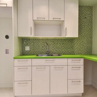 モントリオールの中サイズのモダンスタイルのおしゃれな洗濯室 (ドロップインシンク、フラットパネル扉のキャビネット、淡色木目調キャビネット、人工大理石カウンター、緑の壁、セラミックタイルの床、上下配置の洗濯機・乾燥機、ベージュの床、緑のキッチンカウンター) の写真