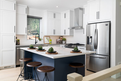 Mid-sized transitional l-shaped light wood floor and brown floor eat-in kitchen photo in Vancouver with a double-bowl sink, shaker cabinets, white cabinets, quartz countertops, white backsplash, subway tile backsplash, stainless steel appliances, an island and white countertops