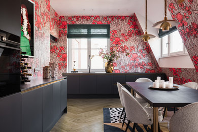 This is an example of a large contemporary l-shaped kitchen/diner in Amsterdam with grey cabinets, medium hardwood flooring, grey worktops, flat-panel cabinets, multi-coloured splashback, black appliances and brown floors.
