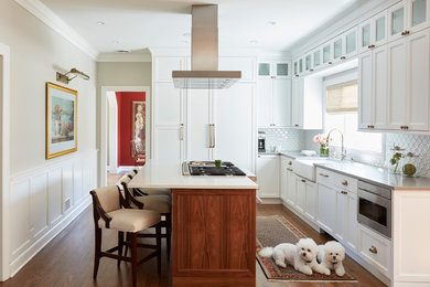 Large traditional l-shaped kitchen in Chicago with a farmhouse sink, shaker cabinets, white cabinets, quartzite benchtops, white splashback, porcelain splashback, panelled appliances, dark hardwood floors, with island and brown floor.