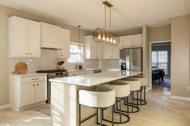 Light wood floor eat-in kitchen photo in Columbus with an undermount sink, shaker cabinets, beige cabinets, quartz countertops, white backsplash, ceramic backsplash, stainless steel appliances, an island and white countertops