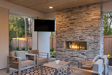 Large beach style concrete back porch idea in Miami with a fireplace and a roof extension