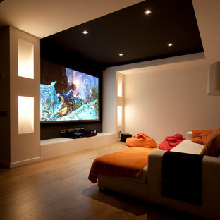 Idée de décoration pour une salle de cinéma design de taille moyenne et fermée avec un mur beige, un sol en bois brun et un écran de projection.