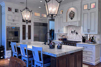 Inspiration for a large timeless u-shaped medium tone wood floor and brown floor eat-in kitchen remodel in Atlanta with a farmhouse sink, raised-panel cabinets, white cabinets, granite countertops, white backsplash, stone tile backsplash, stainless steel appliances, an island and multicolored countertops