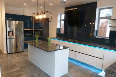This is an example of a large contemporary kitchen in London with a submerged sink, glass-front cabinets, white cabinets, granite worktops, blue splashback, glass sheet splashback, black appliances, porcelain flooring, multiple islands, grey floors and blue worktops.